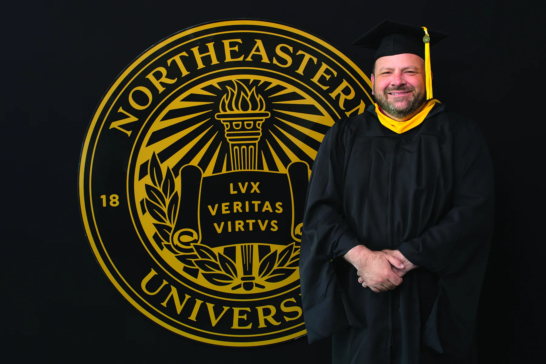 A Roux graduate photographed in front of the Northeastern University seal